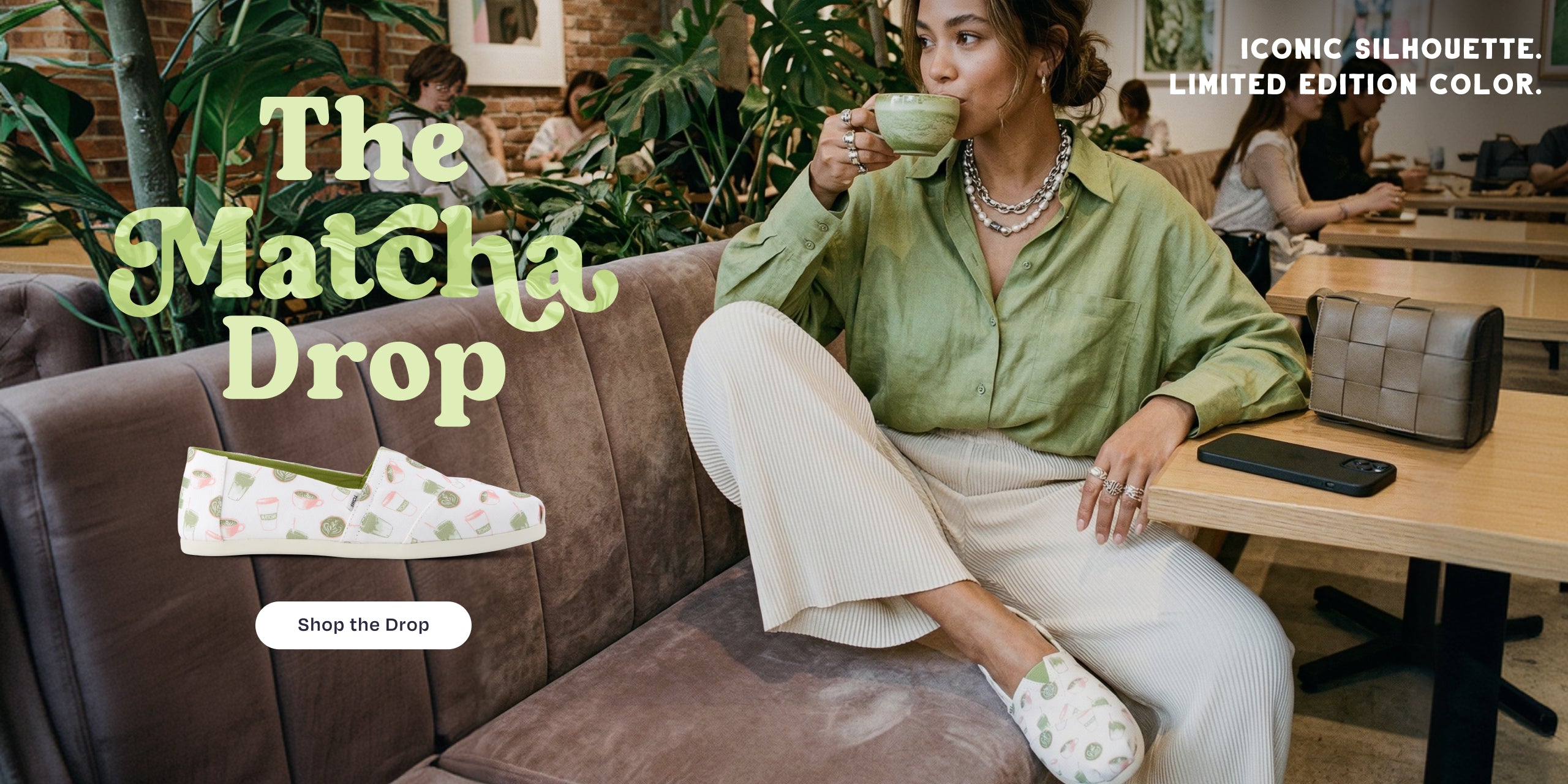 The Matcha Drop. ICONIC SILHOUETTE. LIMITED EDITION COLOR. Shop the Drop: model in cafe sipping from a mug while wearing the Alpargata Classic in Matcha Cafe Print.
